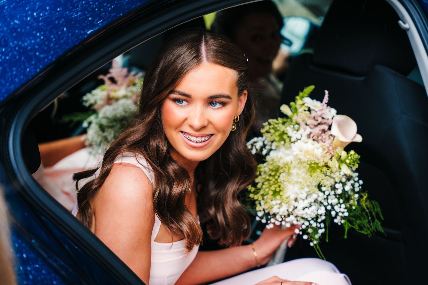 Bride sitting in vintage car holding white and cream floral bouquet at night. The Dean Dublin Wedding Photographer