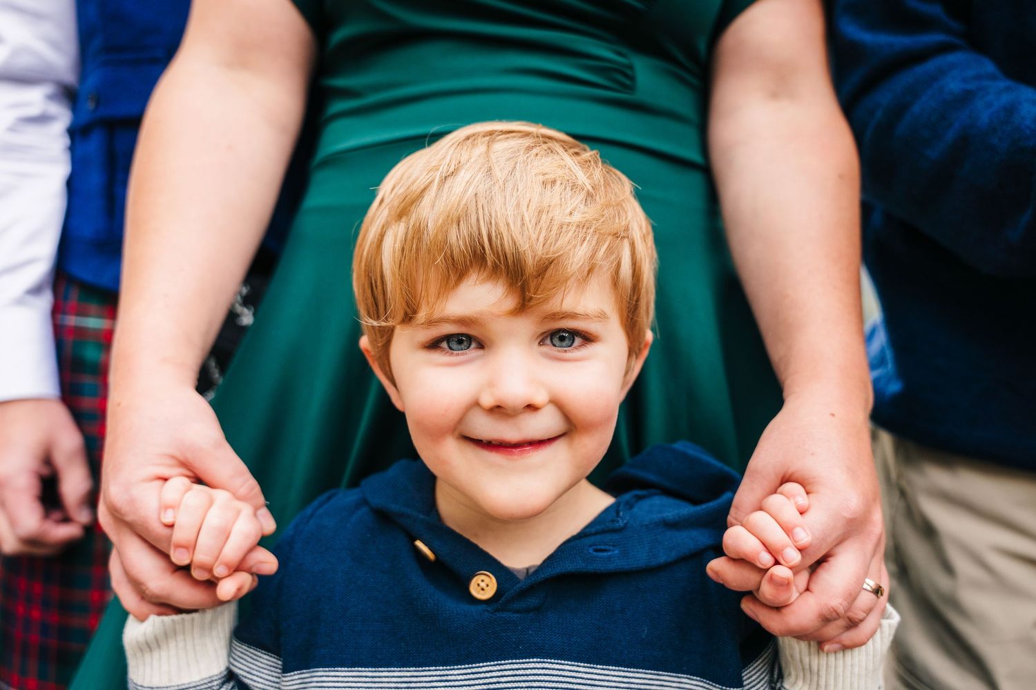 A young child in a navy blue shirt smiles while holding hands with someone wearing a green dress.Family photogrAPHER DUBLIN