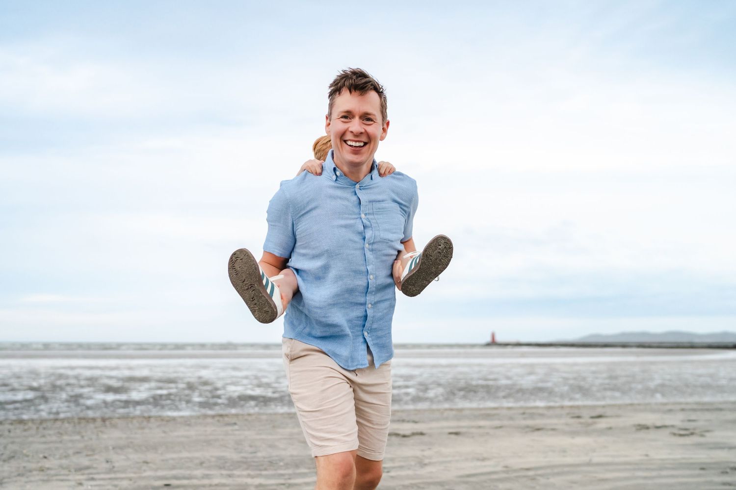 Person in blue shirt and khaki shorts jumping playfully on a beach.  Family photographer Dublin Ireland