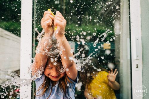 Water splashes and sparkles in sunlight as hands are raised playfully in an energetic summer scene. Family PHOTOGRAPHER Dublin PHOTOGRAPHER