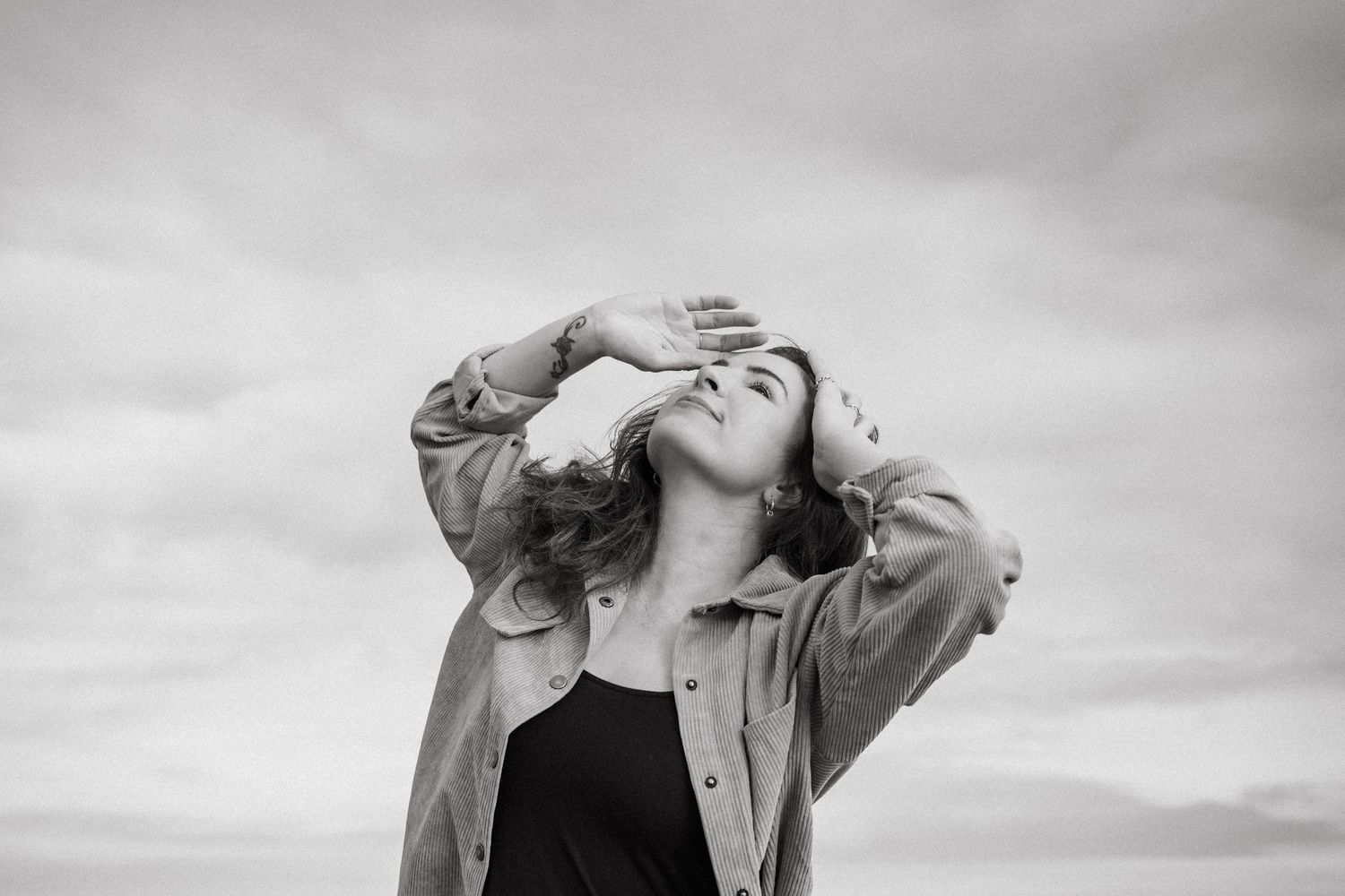 Black and white photo of someone in a jacket tilting their head back against a cloudy sky. PHOTOGRAPHER Dublin ireland