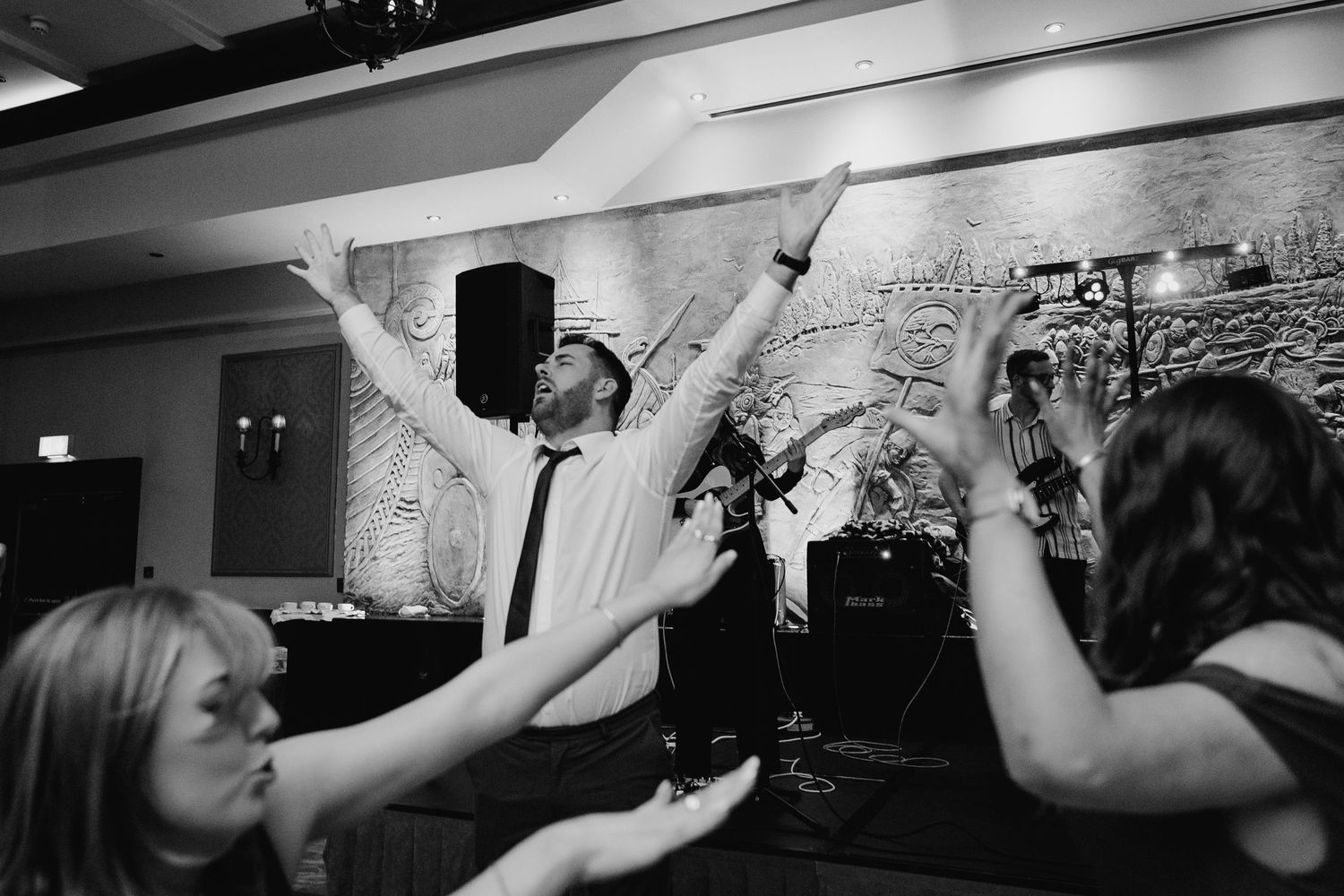 Black and white photo of wedding guests dancing with raised arms at reception party. Wedding photographer dublin