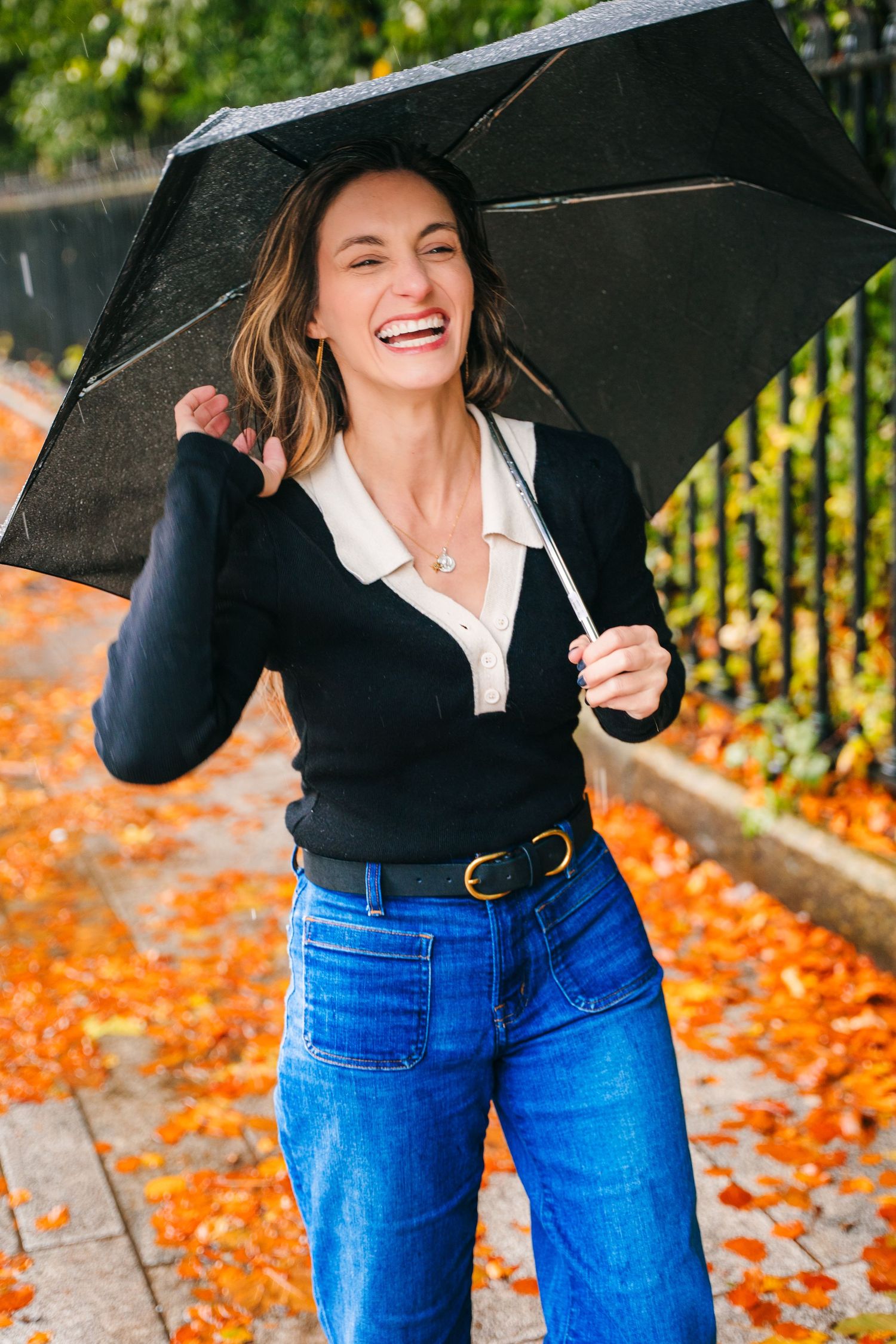 Joyful moment on an autumn day with black umbrella, navy sweater and jeans among scattered orange leaves. Headshots Dublin Photographer Port