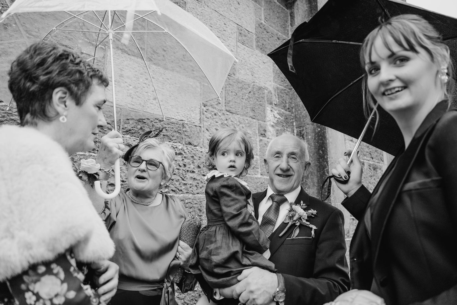 Black and white candid shots of wedding guests sharing joyful moments under umbrellas.