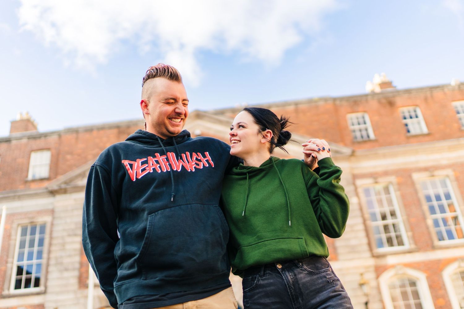 A couple shares a joyful moment together outside a historic brick building on a sunny day. PHOTOGRAPHER Dublin Ireland