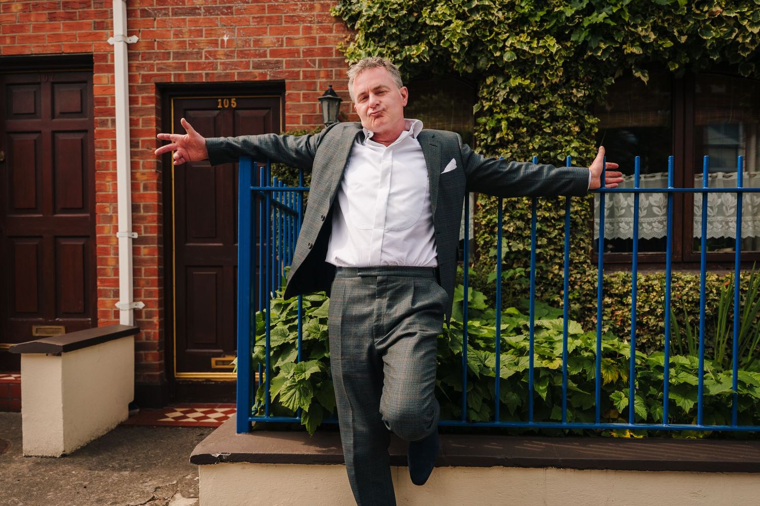 Playful portrait session of wedding party members in front of brick building with blue railings. Same sex wedding PHOTOGRAPHER Dublin