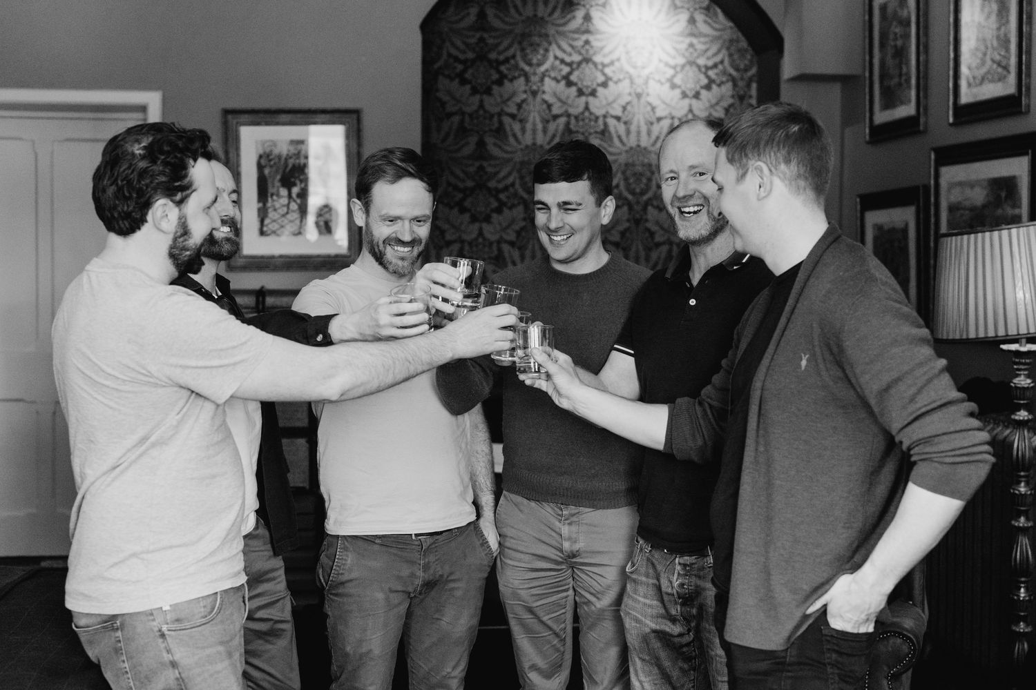 Castle Leslie Wedding Photographer Dublin A group of friends toast and clink their drinks together in a dark room with framed photos.