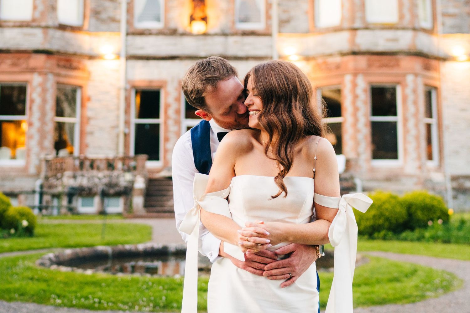 Castle Leslie Wedding Photographer Dublin Wedding couple embraces in front of historic stone building with beautiful window details.