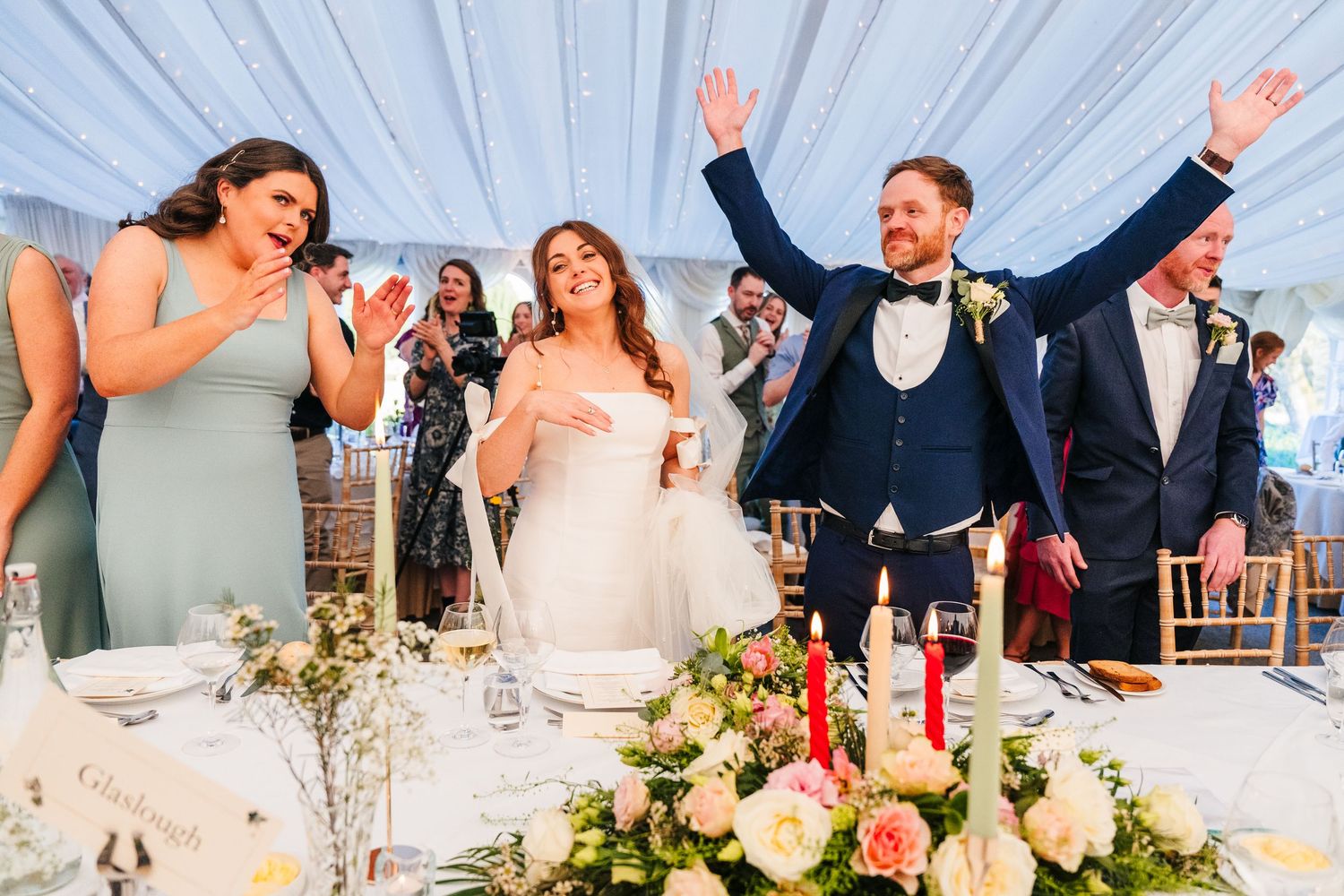 Castle Leslie Wedding PhotA candid celebration moment at a wedding reception with guests standing and cheering under elegant white draping.