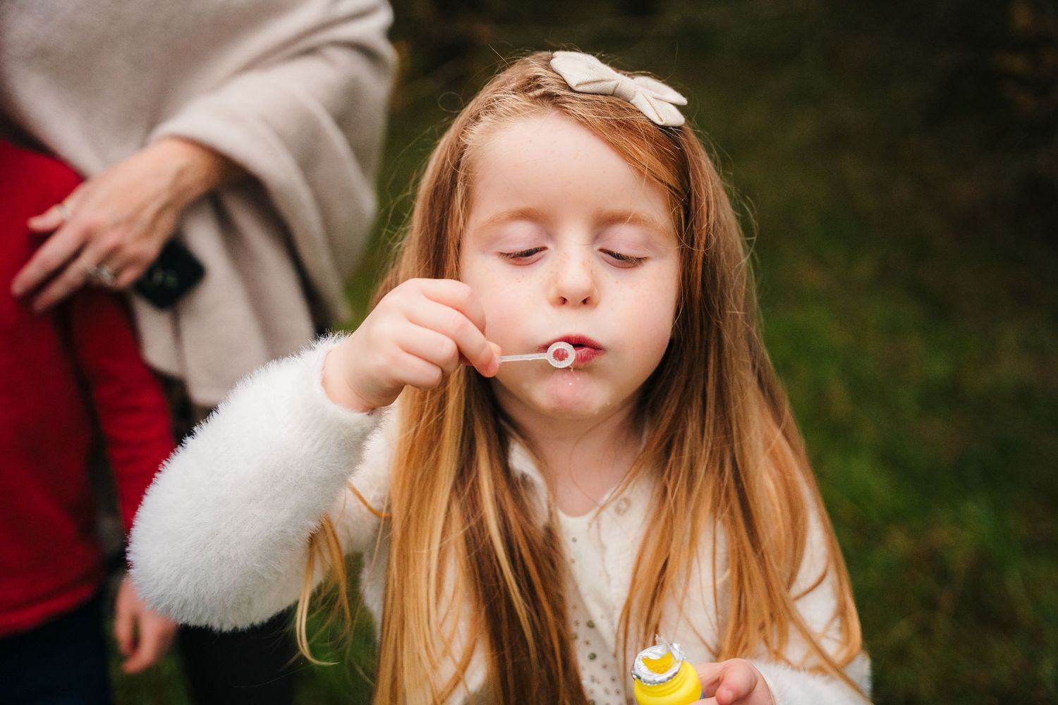 Girl in white sweater blowing bubbles outdoors during autumn photoshoot.