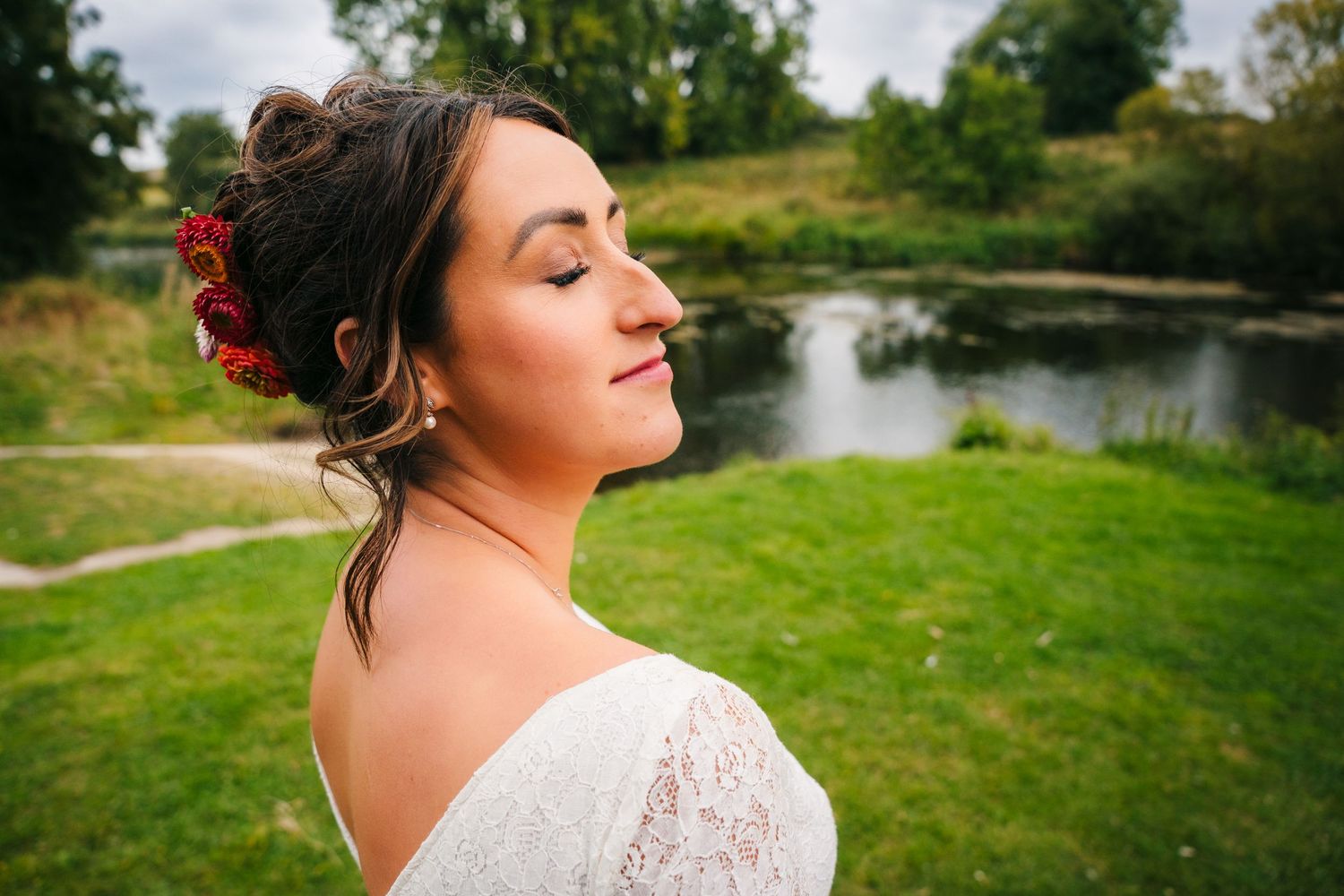 A bride in a white lace dress poses in a scenic outdoor setting with a lake and green landscape. Wedding Photography Trim Castle Ireland
