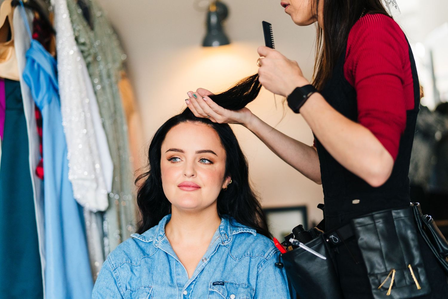 Woman in blue denim shirt looking thoughtful while sorting through closet of hanging clothes. House Dublin Wedding Photographer