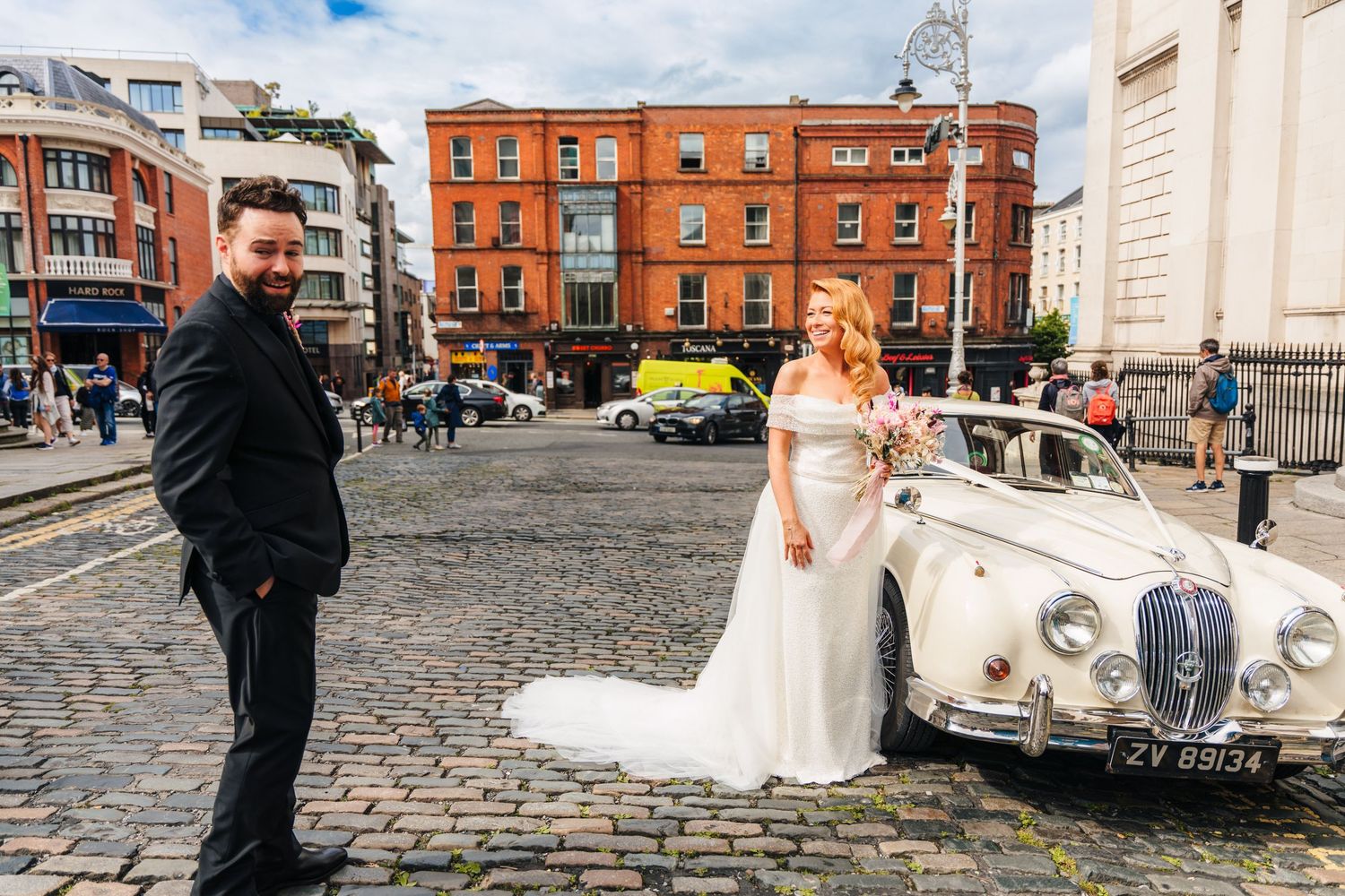 Wedding party and vintage car on cobblestone street with historic brick buildings in background.  city hall dublin wedding photos