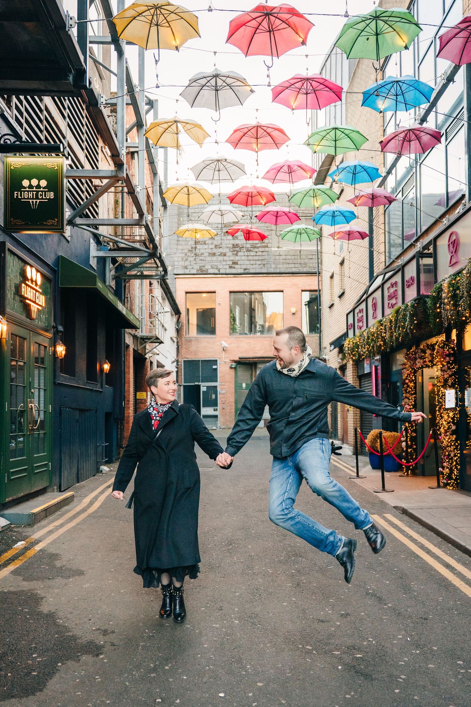 Colorful umbrellas hang above a charming street with people dancing and posing beneath them. family PHOTOGRAPHER Dublin