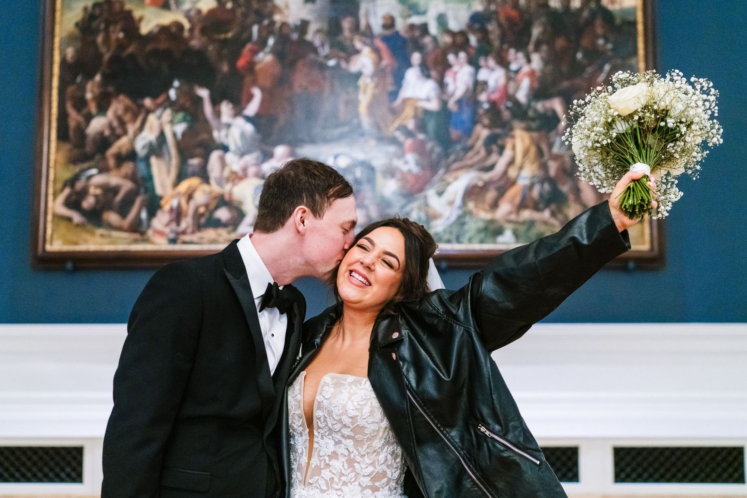 A couple in formal wedding attire share a romantic dance in front of framed artwork on a blue wall. Wedding Photographer Dublin Ireland