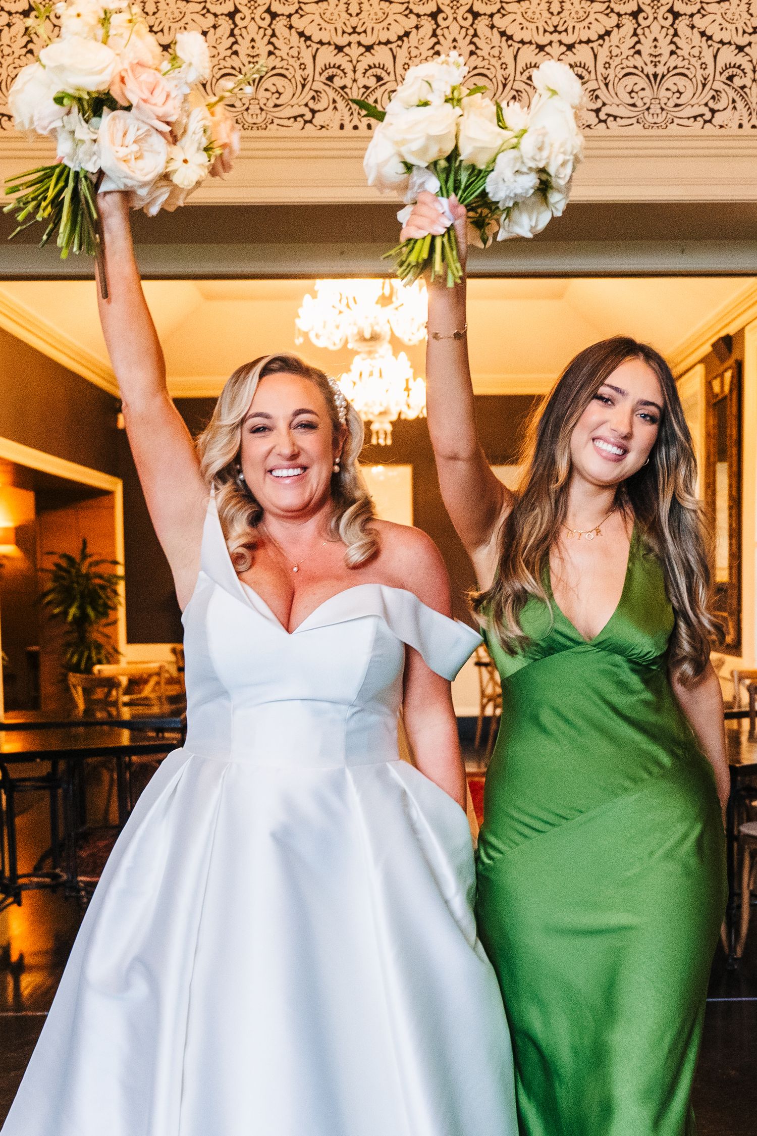 Wedding party members in white and emerald green dresses holding bouquets in celebration at an indoor venue.  Virginia Park Lodge Wedding Ph