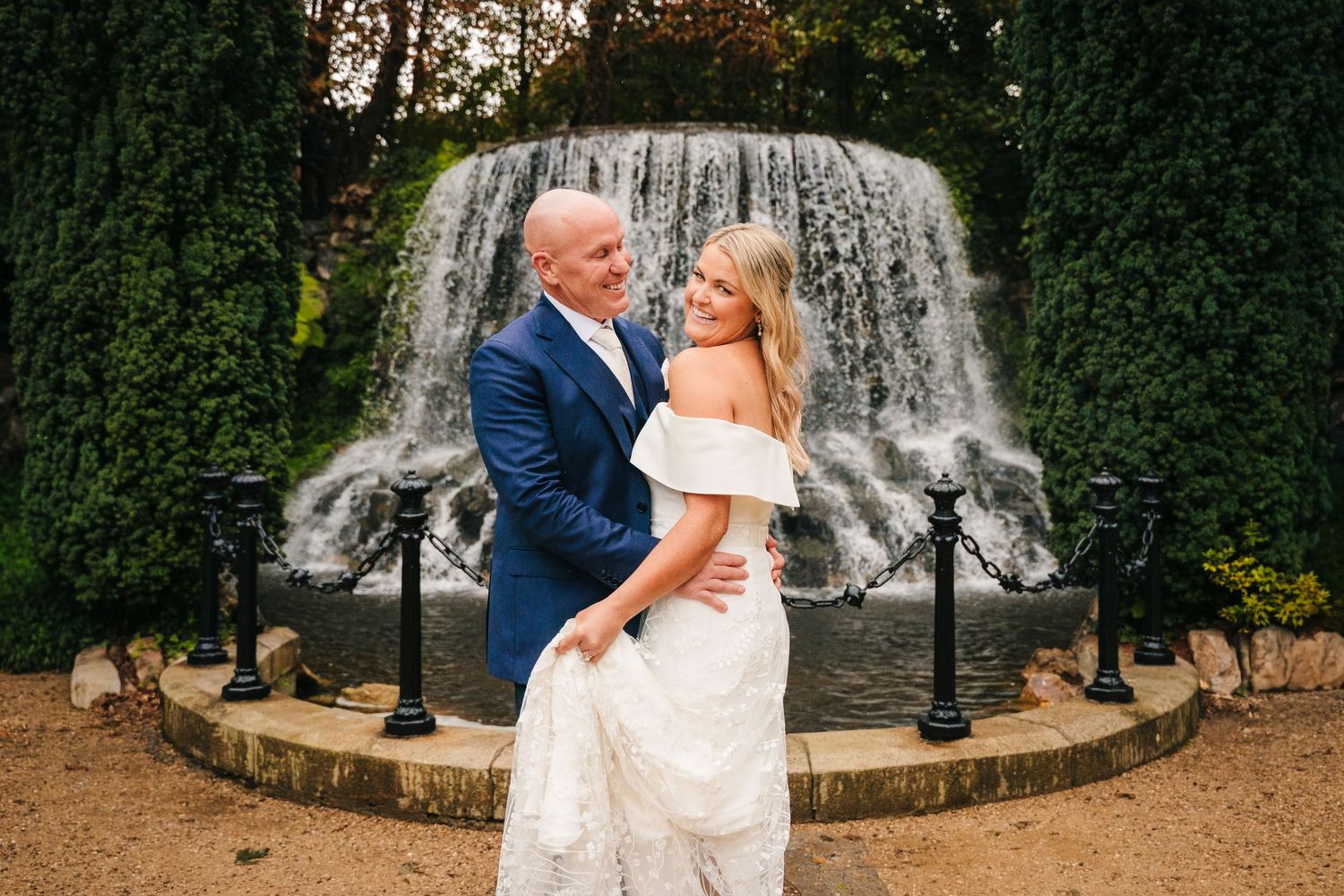 Wedding couple photographs in front of a grand fountain with lush greenery and garden scenery. The Dean Dublin Wedding Photographer