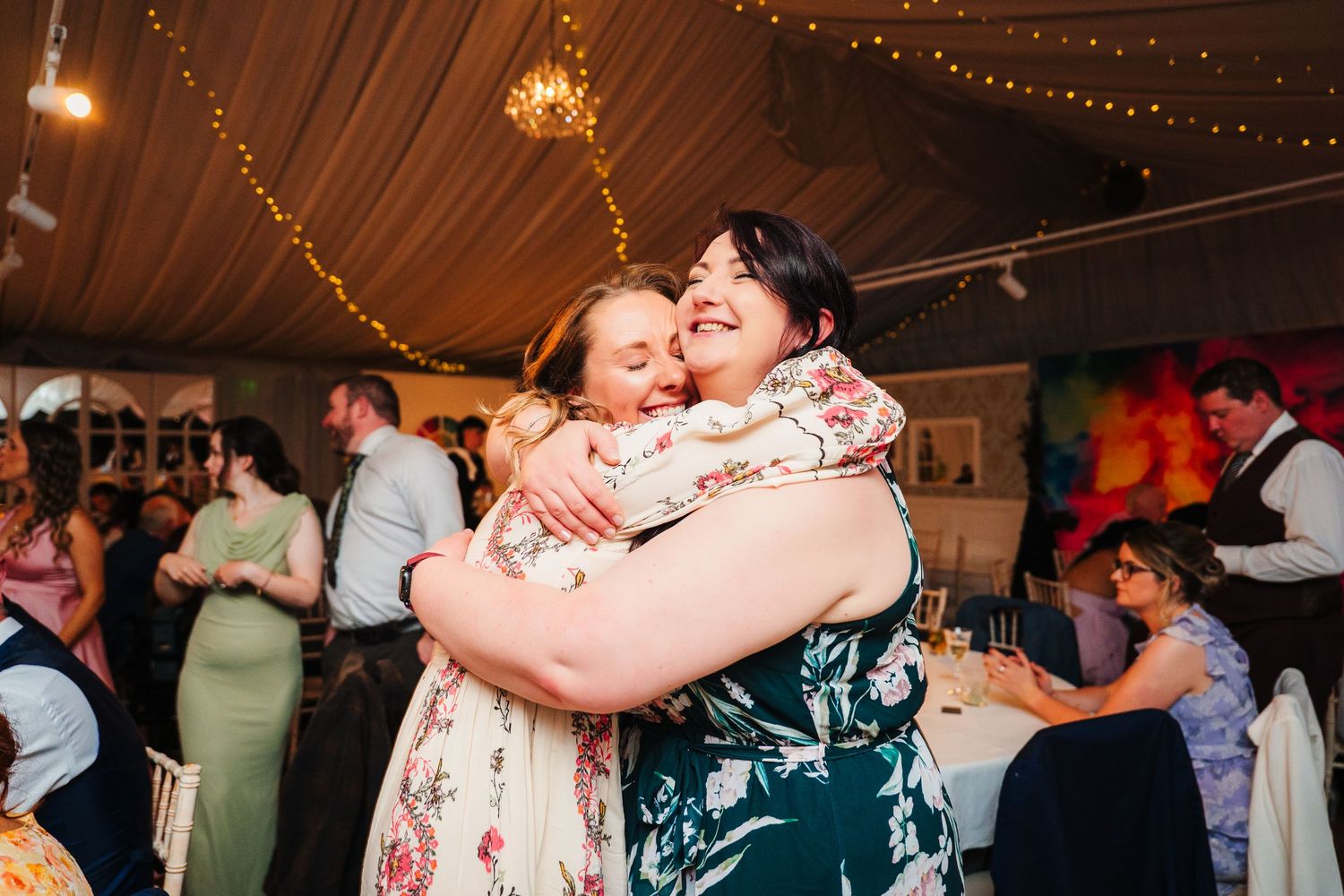 Two wedding guests share an emotional embrace on the dance floor under string lights. LGBTQ Ashley Park Wedding Photographer
