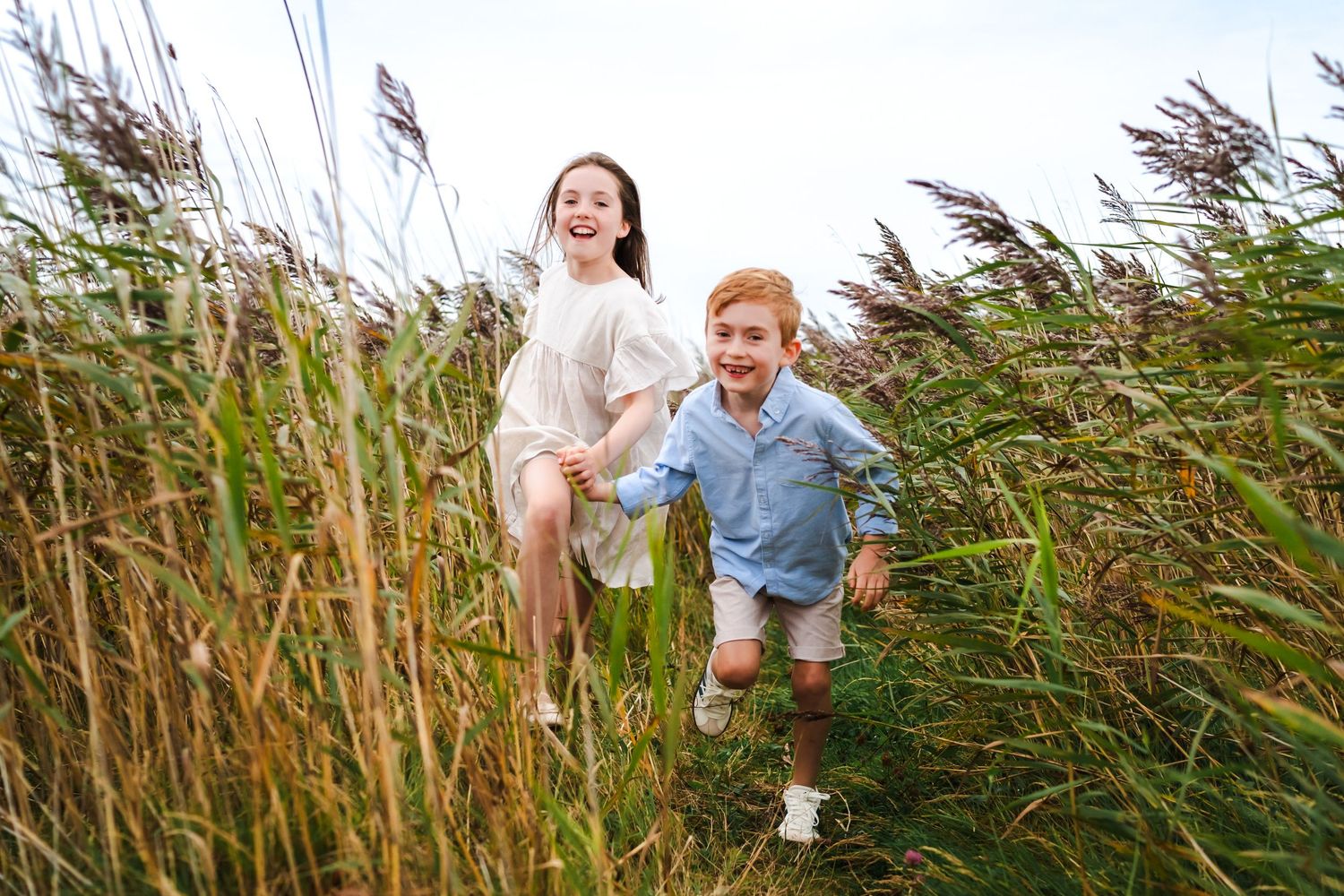 Candid photograph of a joyful child running through tall swaying grass in a meadow on a summer day.  Family photographer Dublin Ireland