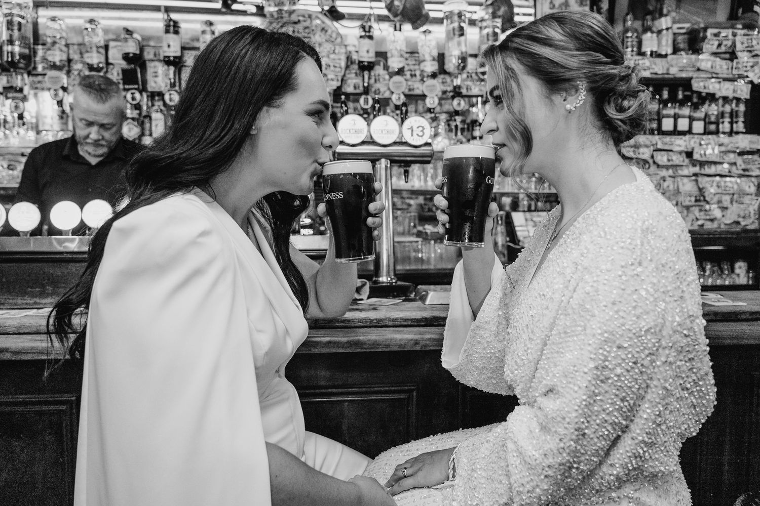 Two people in white attire share an emotional moment at a bar counter. House Dublin Wedding Photographer