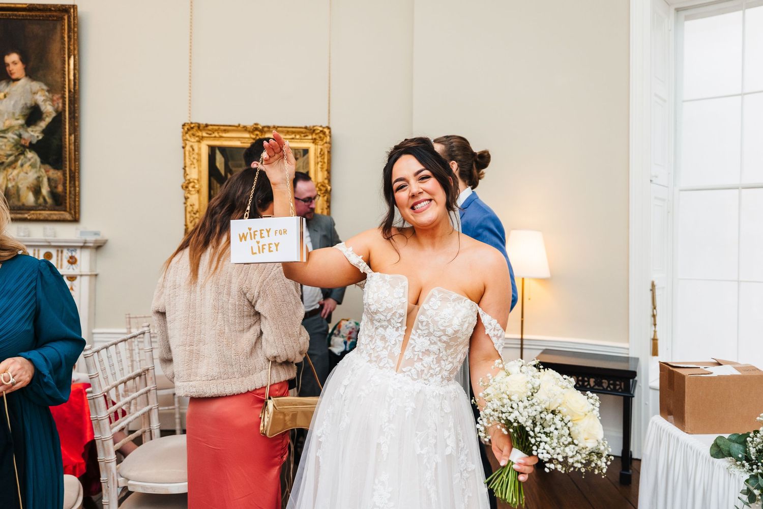A bride in a white dress smiles and gestures during candid wedding reception moments. Wedding PHOTOGRAPHER Dublin