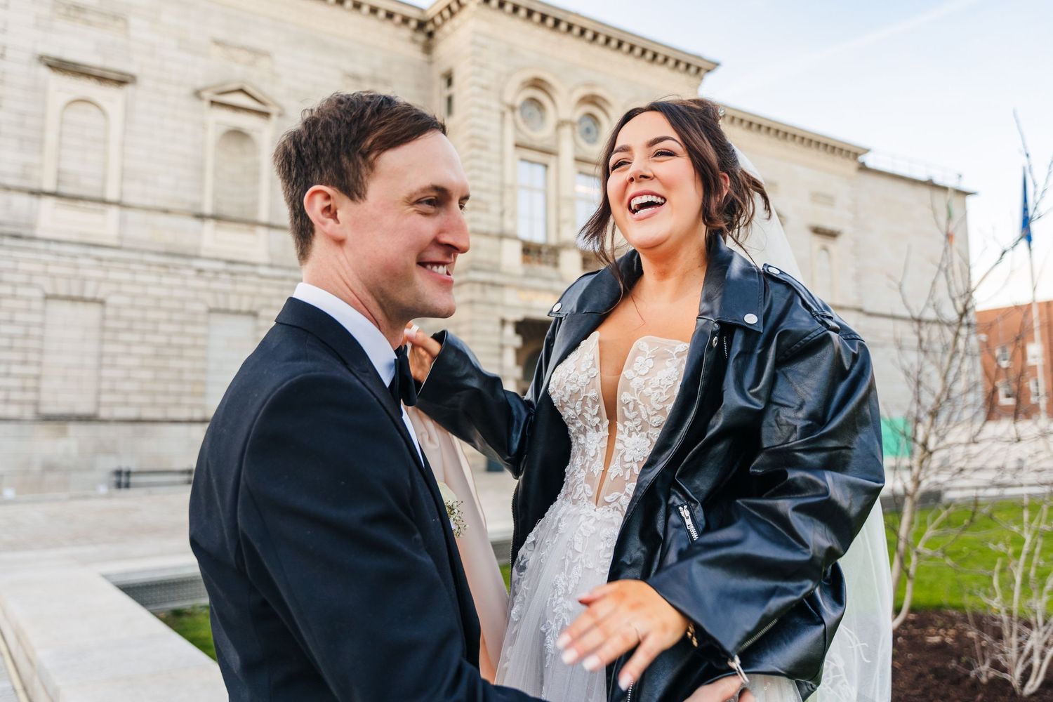 A joyful wedding couple shares a candid laughing moment outside a stone building. Wedding PHOTOGRAPHER Dublin