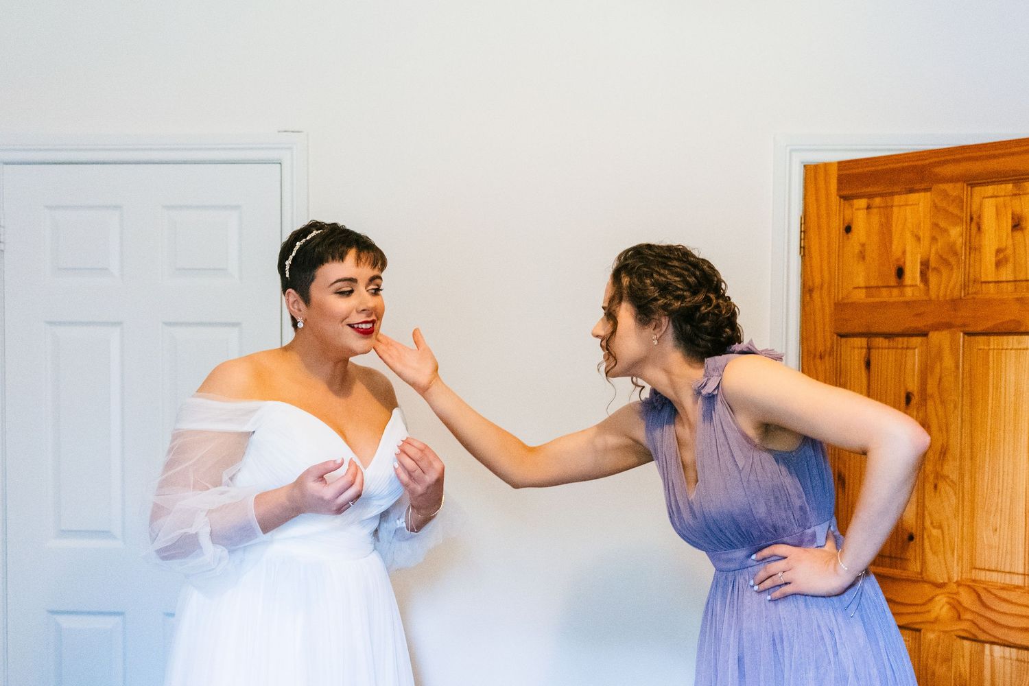 Two people share a candid moment of laughter together in a room, one wearing a white dress and another in purple.Millhouse slane wedding pho