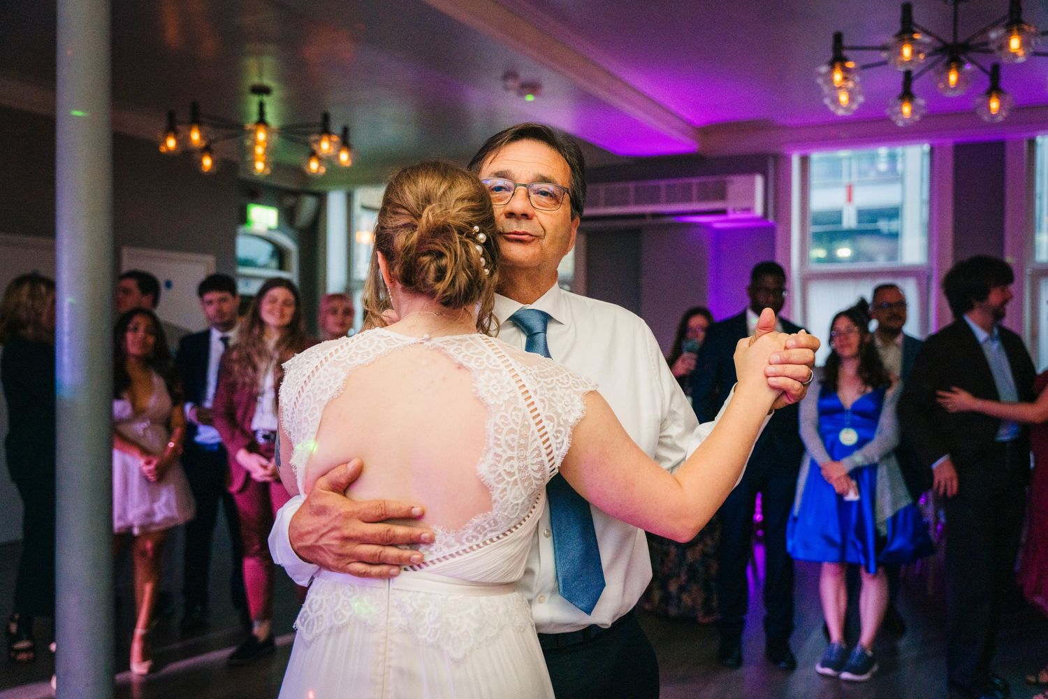 Couples dancing at an evening wedding reception with purple ambient lighting and hanging fixtures. PHOTOGRAPHER Dublin Ireland Wedding