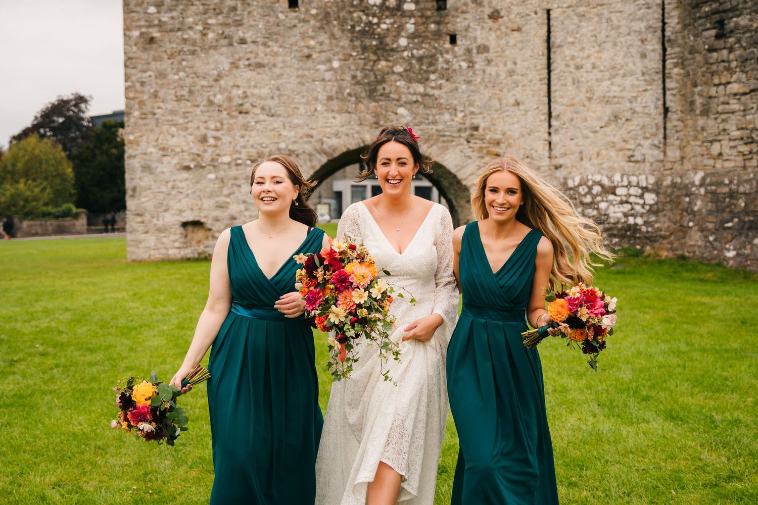 Wedding party in emerald green dresses and white gown pose on grassy lawn. Wedding Photography Trim Castle Ireland