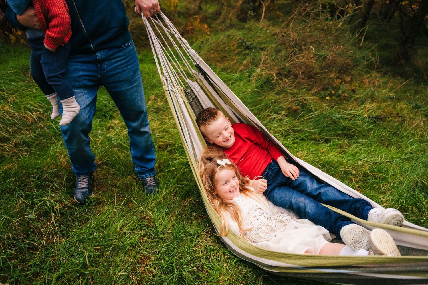 Family Photographer Dublin Ireland  Family members play and relax on a hammock in a lush green outdoor setting.