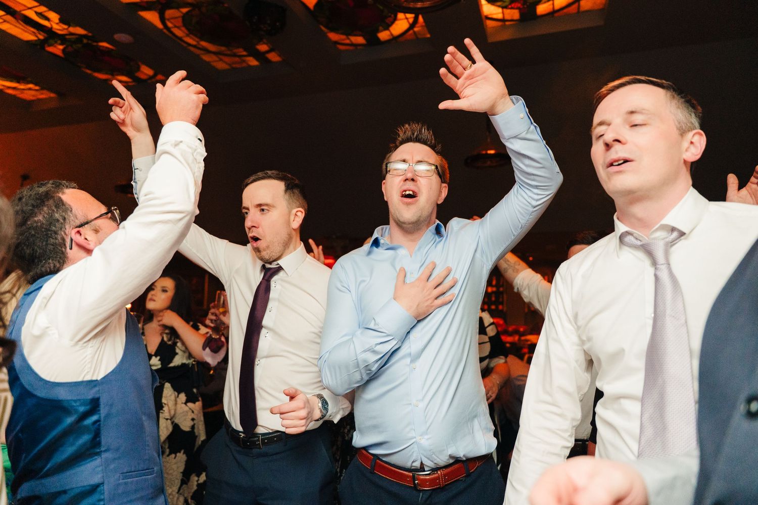 Wedding guests dancing with enthusiasm under warm lighting at the reception. Marco Pierre Dublin Wedding Photographer