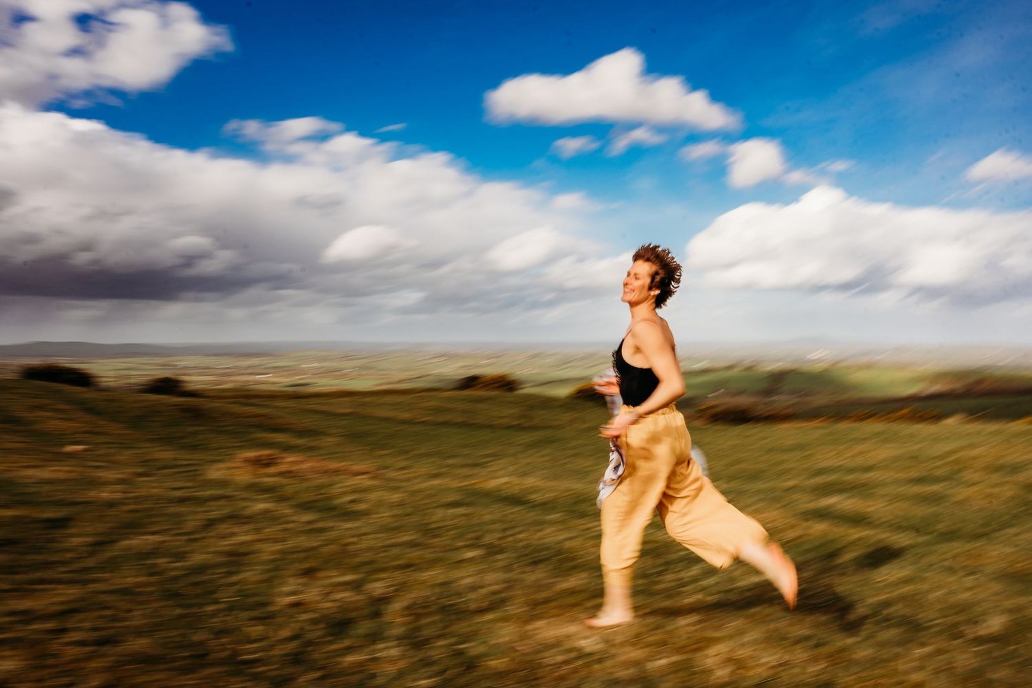 Runner in athletic wear moving across a grassy plain under a dramatic blue sky with white clouds. Portrait PHOTOGRAPHER Dublin