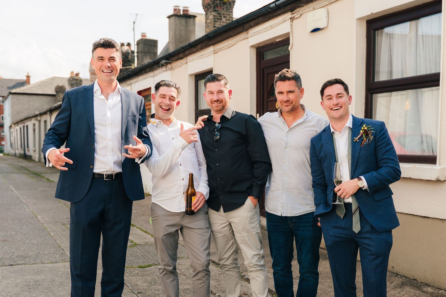 Groomsmen laughing and celebrating together on residential street during wedding. Same sex wedding PHOTOGRAPHER Dublin