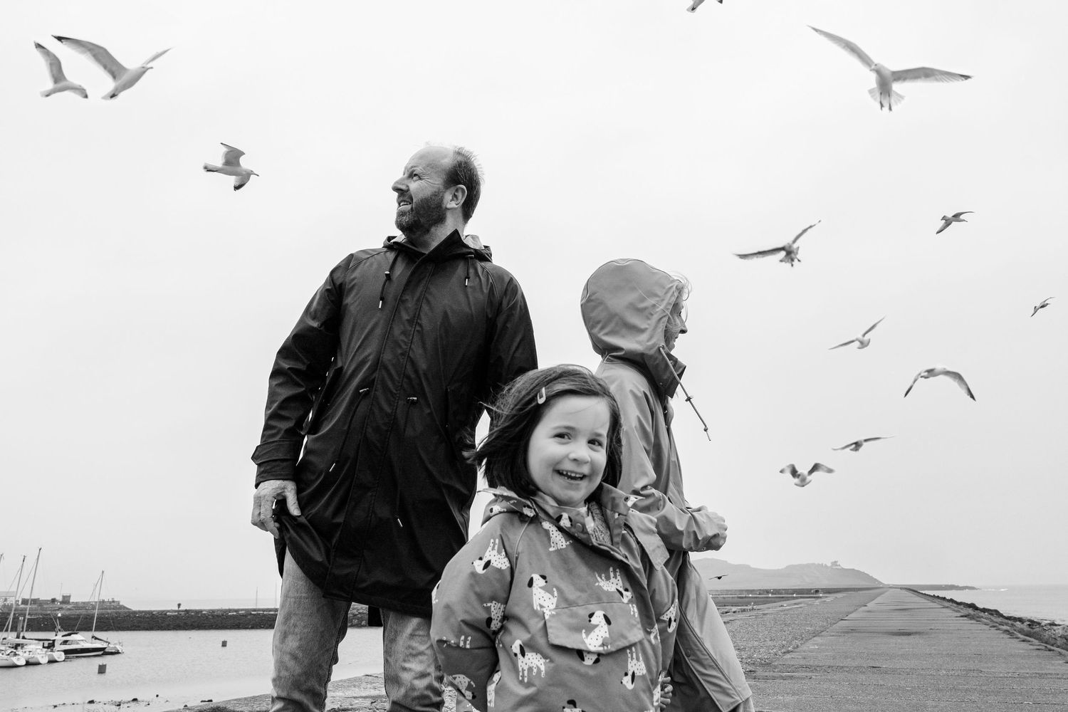 Black and white photo of a family standing together at a beach with seagulls flying overhead. PHOTOGRAPHER Dublin