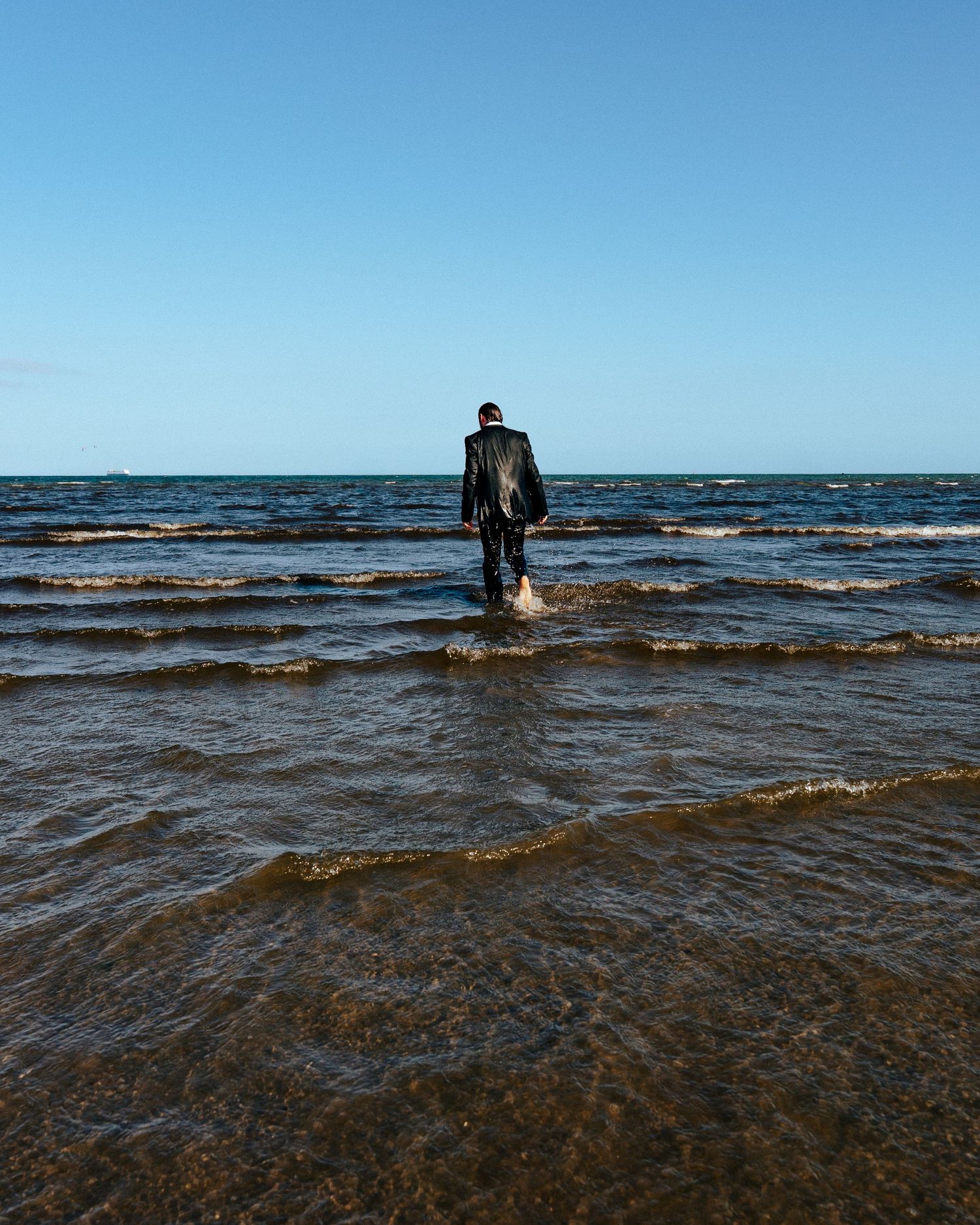 Distant figures wading in the dark blue waters of the ocean under a clear sky. PHOTOGRAPHER Dublin