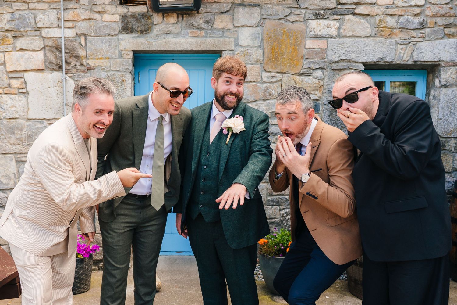 Five groomsmen in suits pose playfully outside a stone building. . Village Barn Tyrrellspass wedding photographer Ireland