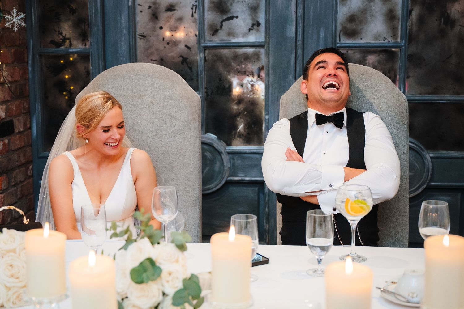 Wedding party sits at an elegantly decorated reception table with glowing candles and white floral arrangements.