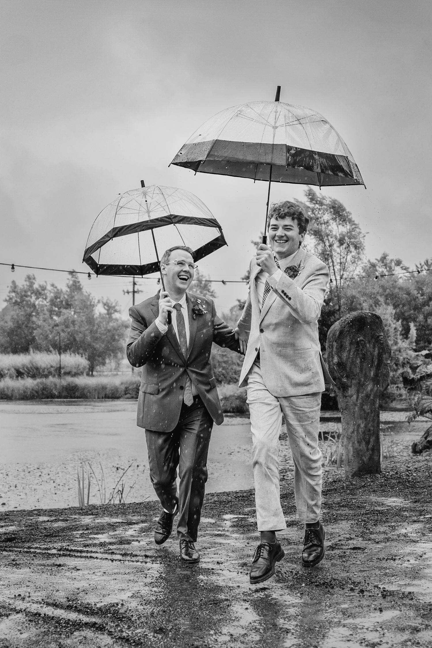 Wedding party members running with clear umbrellas in the rain, captured in black and white. Wedding photographer Dublin