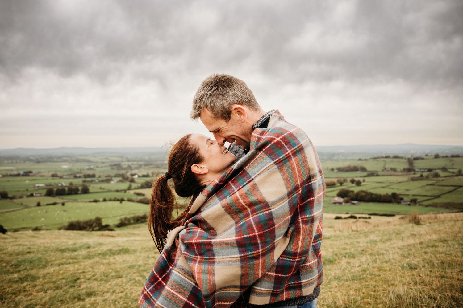 Two people share a romantic embrace on a hilltop overlooking a scenic countryside landscape. PHOTOGRAPHER Dublin ireland Photographer dublin