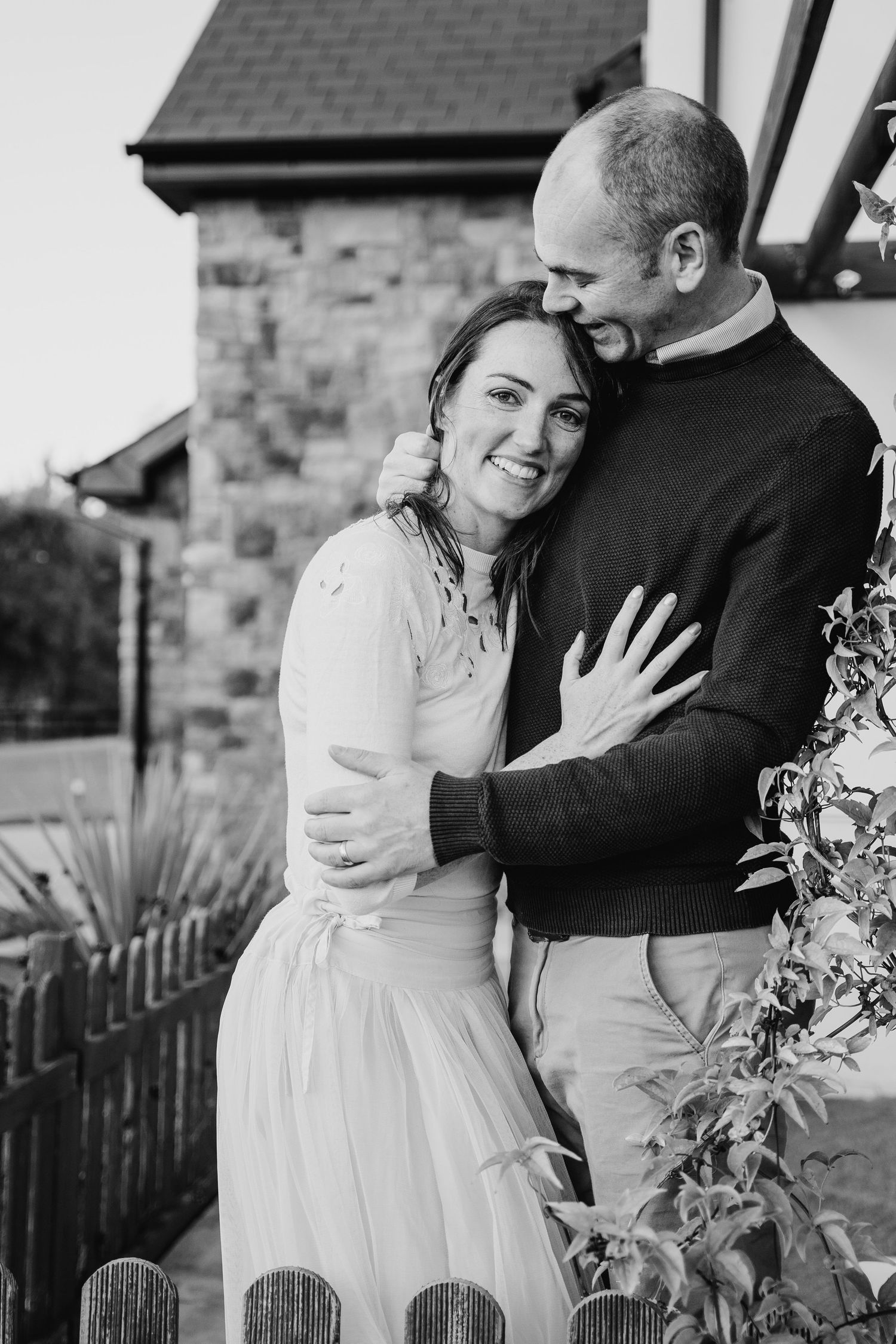A romantic black and white photo series shows a couple embracing and laughing together outdoors near a stone wall. PHOTOGRAPHER Dublin irela