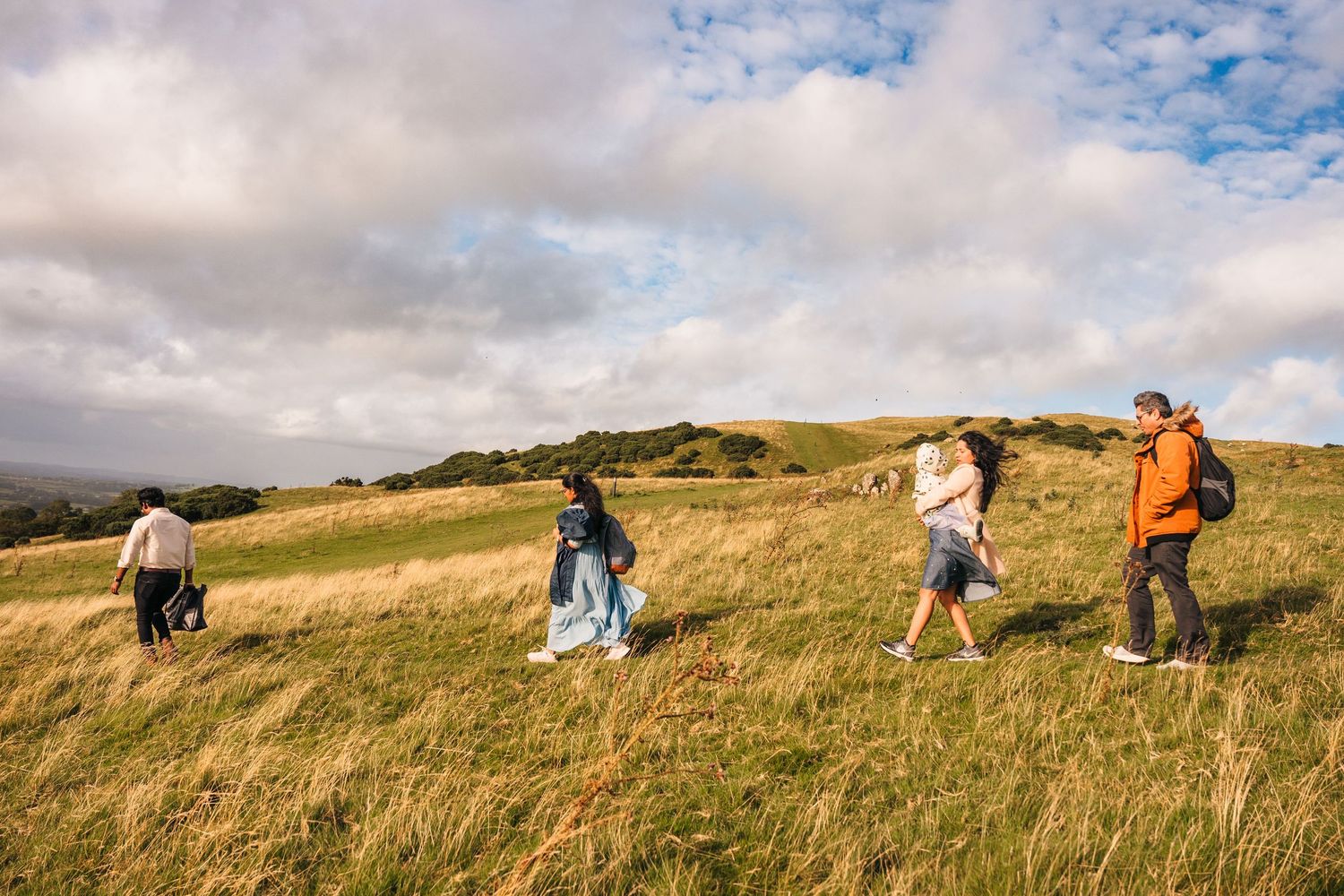 Group of hikers traverse a scenic grassy hillside trail under a partly cloudy sky on a sunny day. family PHOTOGRAPHER Dublin
