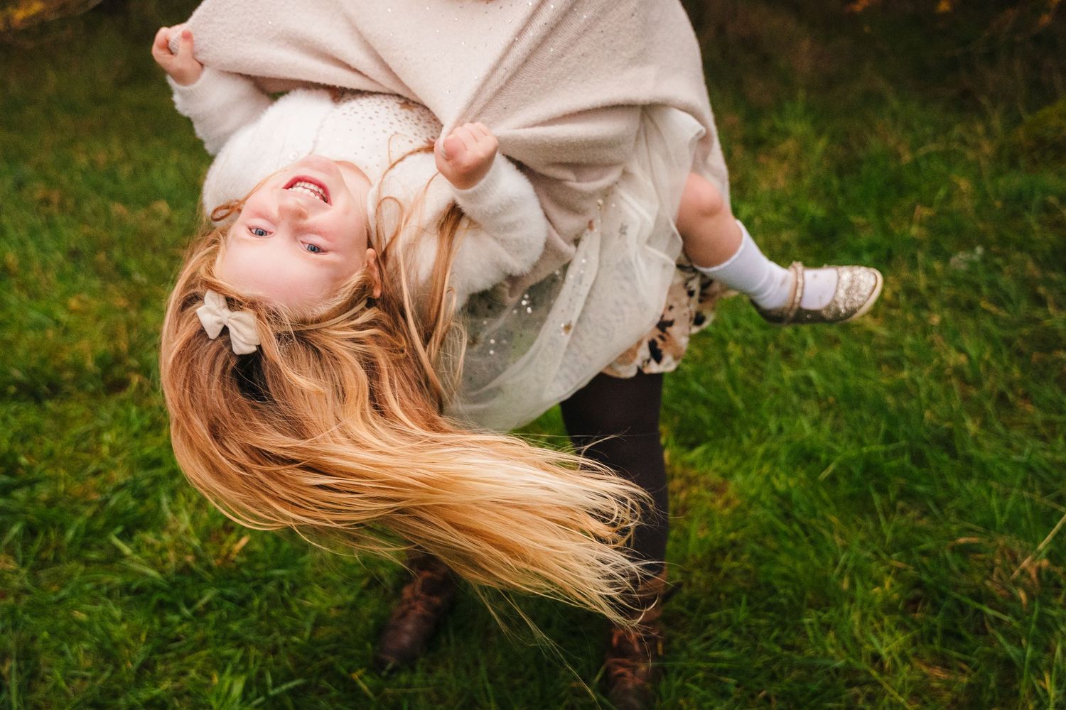 A person in a flowy cream dress spins joyfully in a green grassy field during golden hour. family PHOTOGRAPHER Dublin
