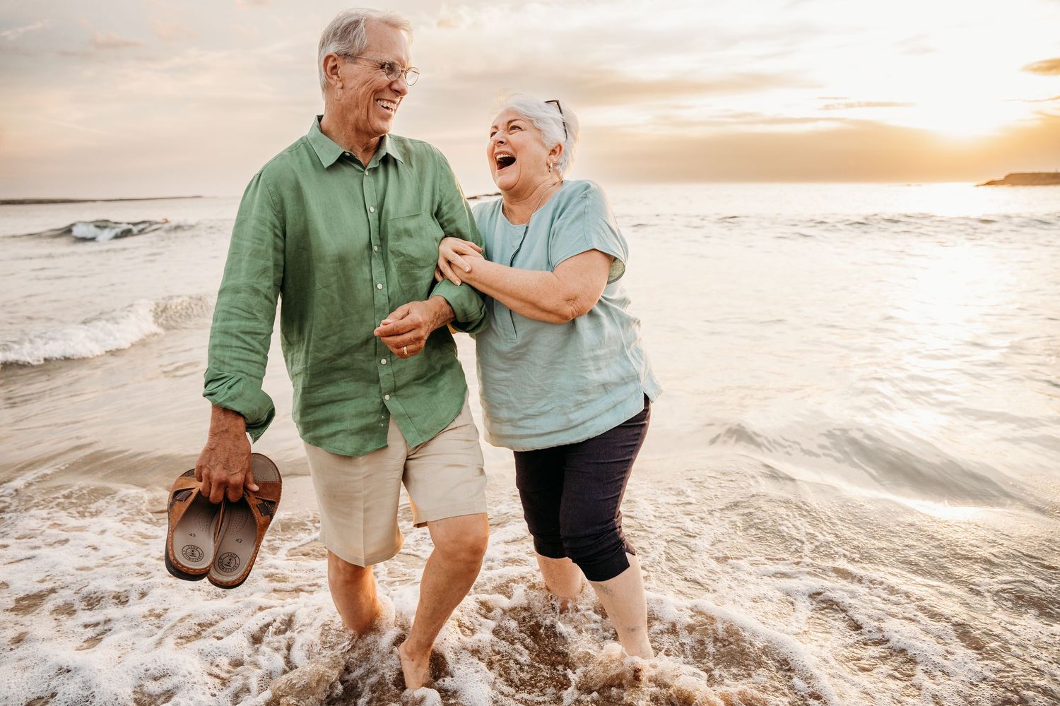 Retired couple walking and laughing together on a beach at sunset. PHOTOGRAPHER Dublin ireland