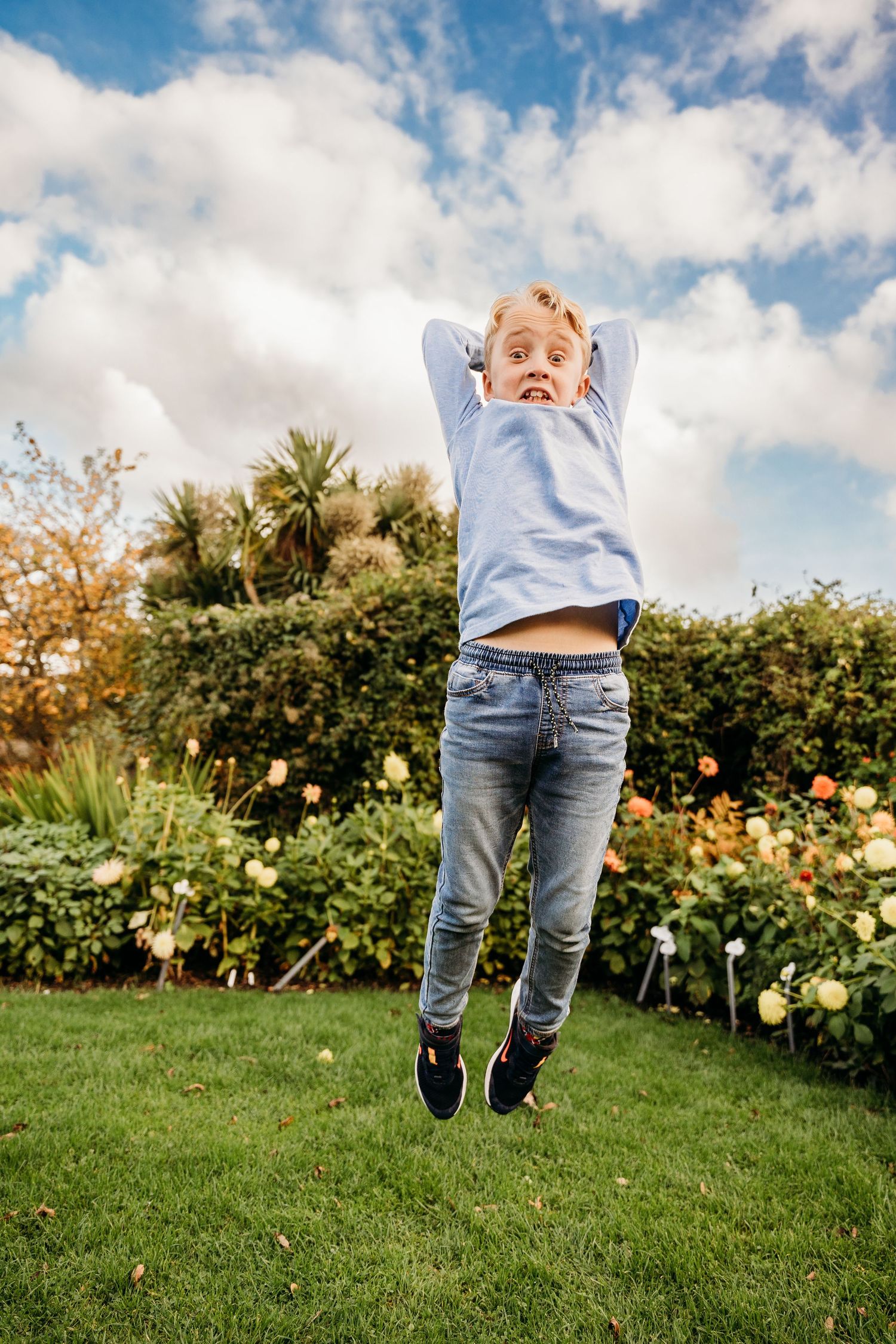 Joyful child jumping high in a garden with blooming flowers and fluffy clouds in the blue sky. family PHOTOGRAPHER Dublin
