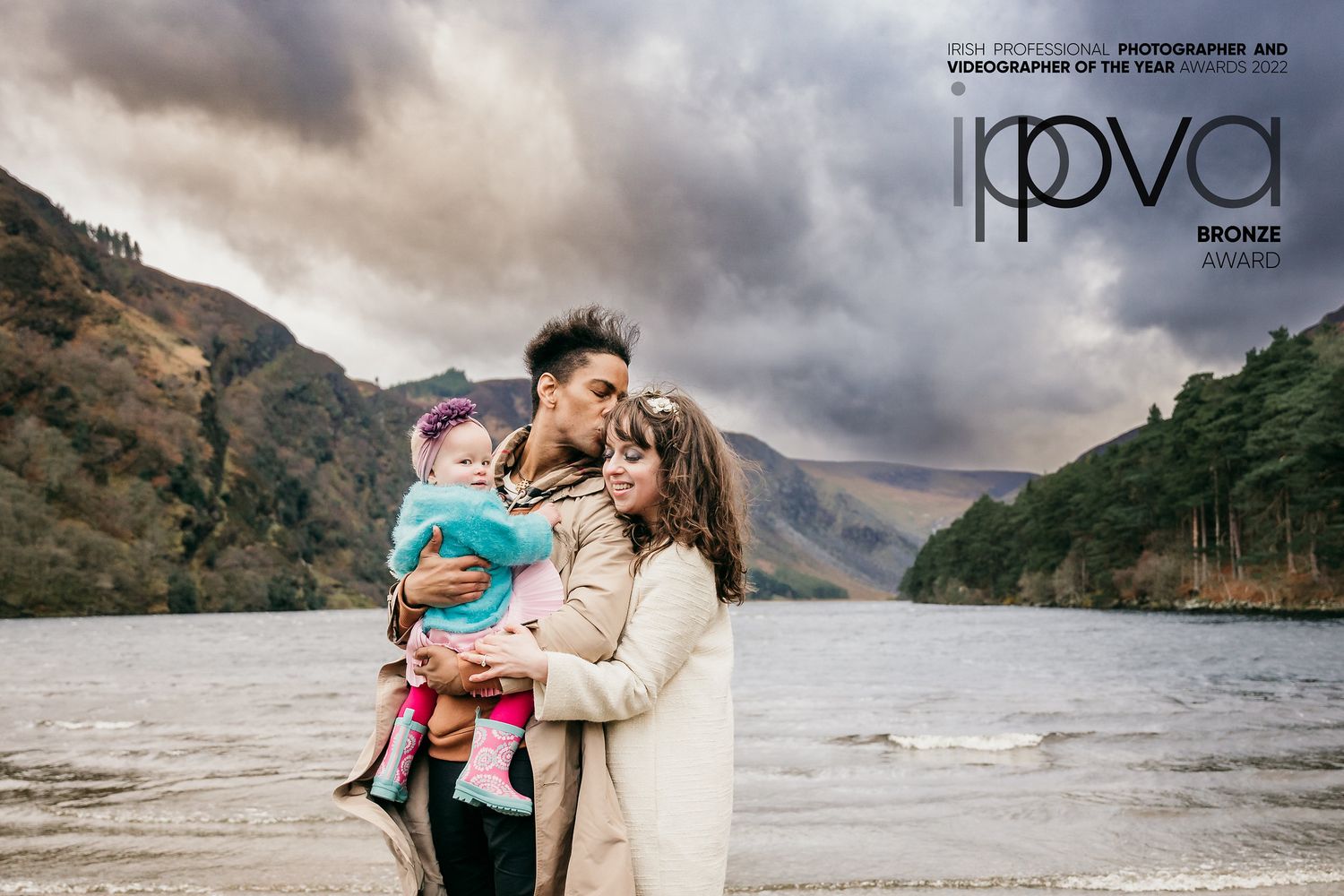 A scenic family moment at a lake with dramatic cloudy mountain backdrop. Family PHOTOGRAPHER Dublin