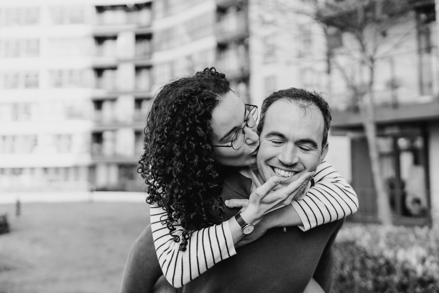 Black and white photo of a romantic couple sharing a tender embrace outdoors near city buildings. PHOTOGRAPHER Dublin ireland