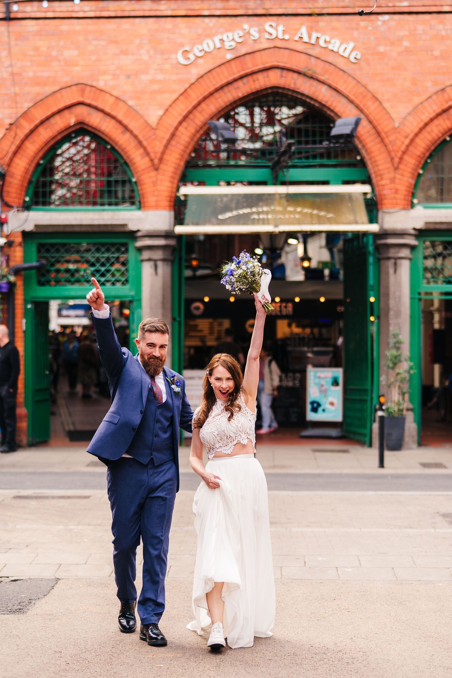 A happy couple celebrates outside the historic red brick arches of George's Street Arcade in Dublin. Wedding PHOTOGRAPHER Dublin