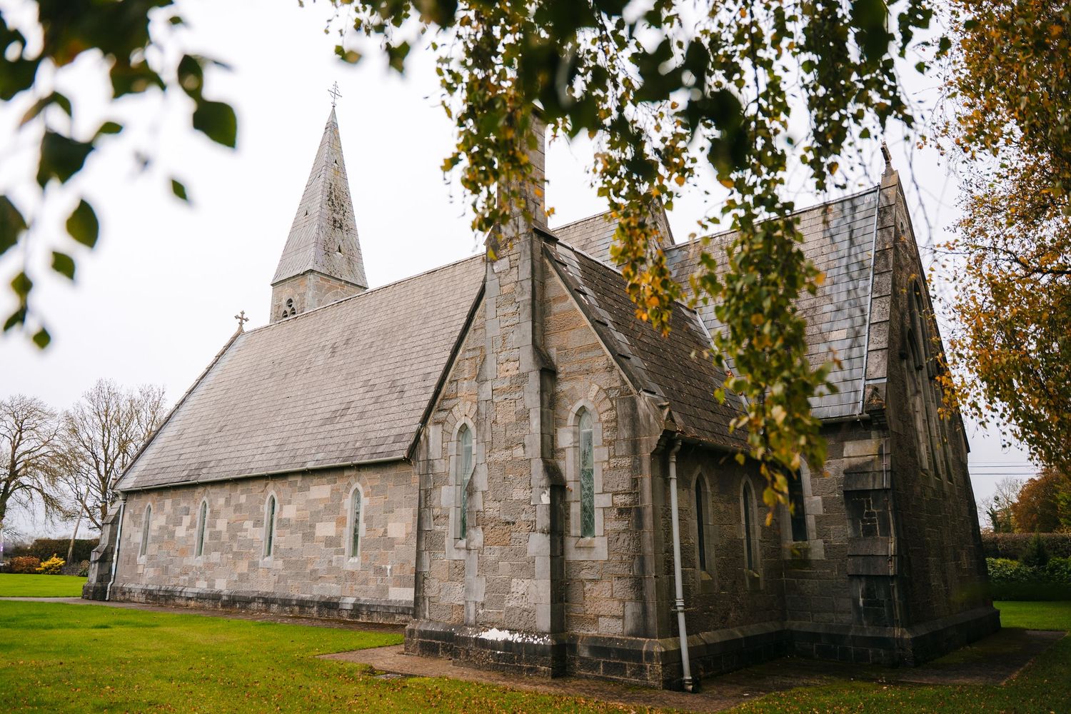 Stone church exterior with gothic architecture and spires surrounded by autumn trees.
