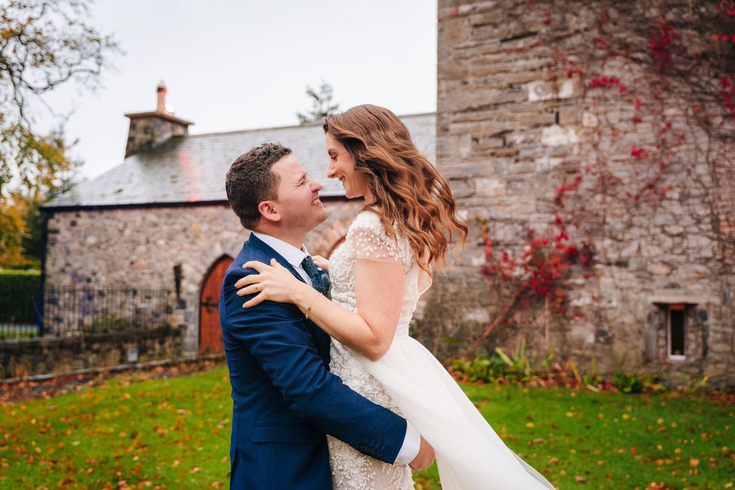 Couple shares romantic moment against rustic stone wall with red autumn vines.