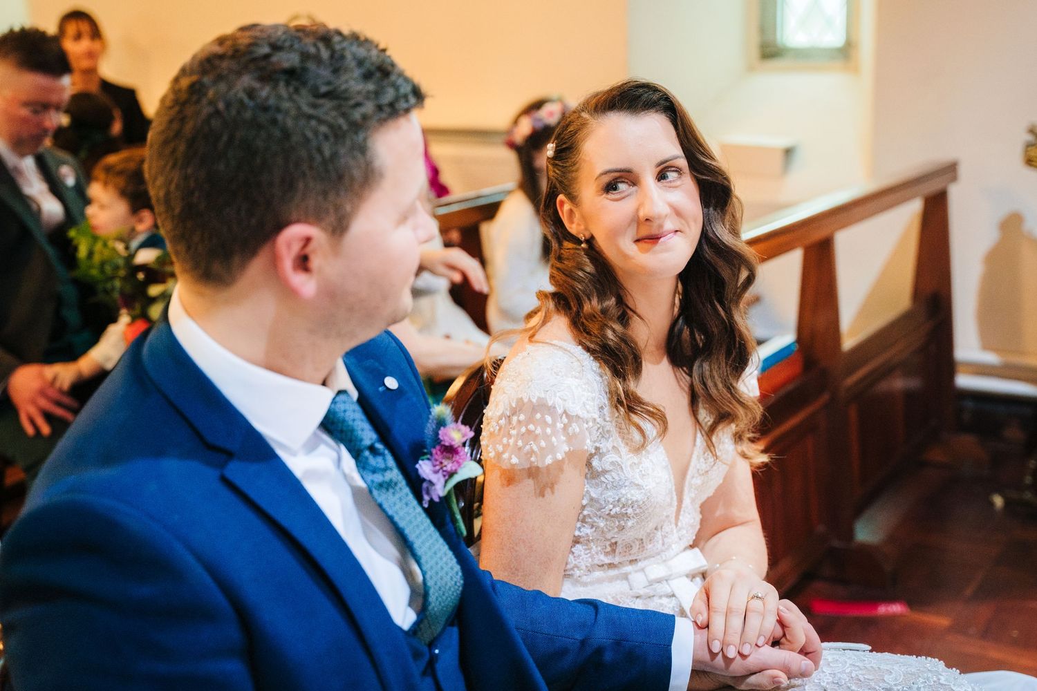 Wedding guests fill wooden church pews during an intimate ceremony with natural lighting.